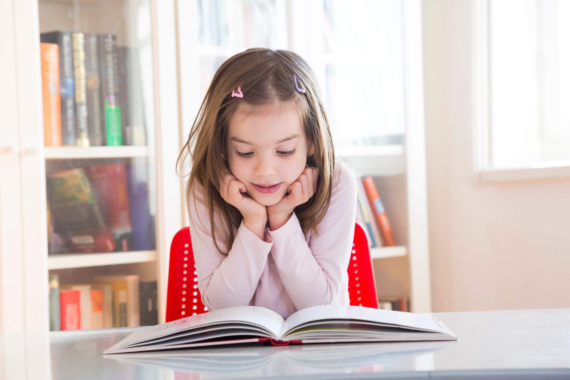 A young girl sat at a table, reading a book.