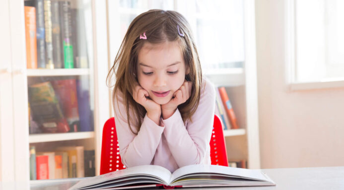 A young girl sat at a table, reading a book.