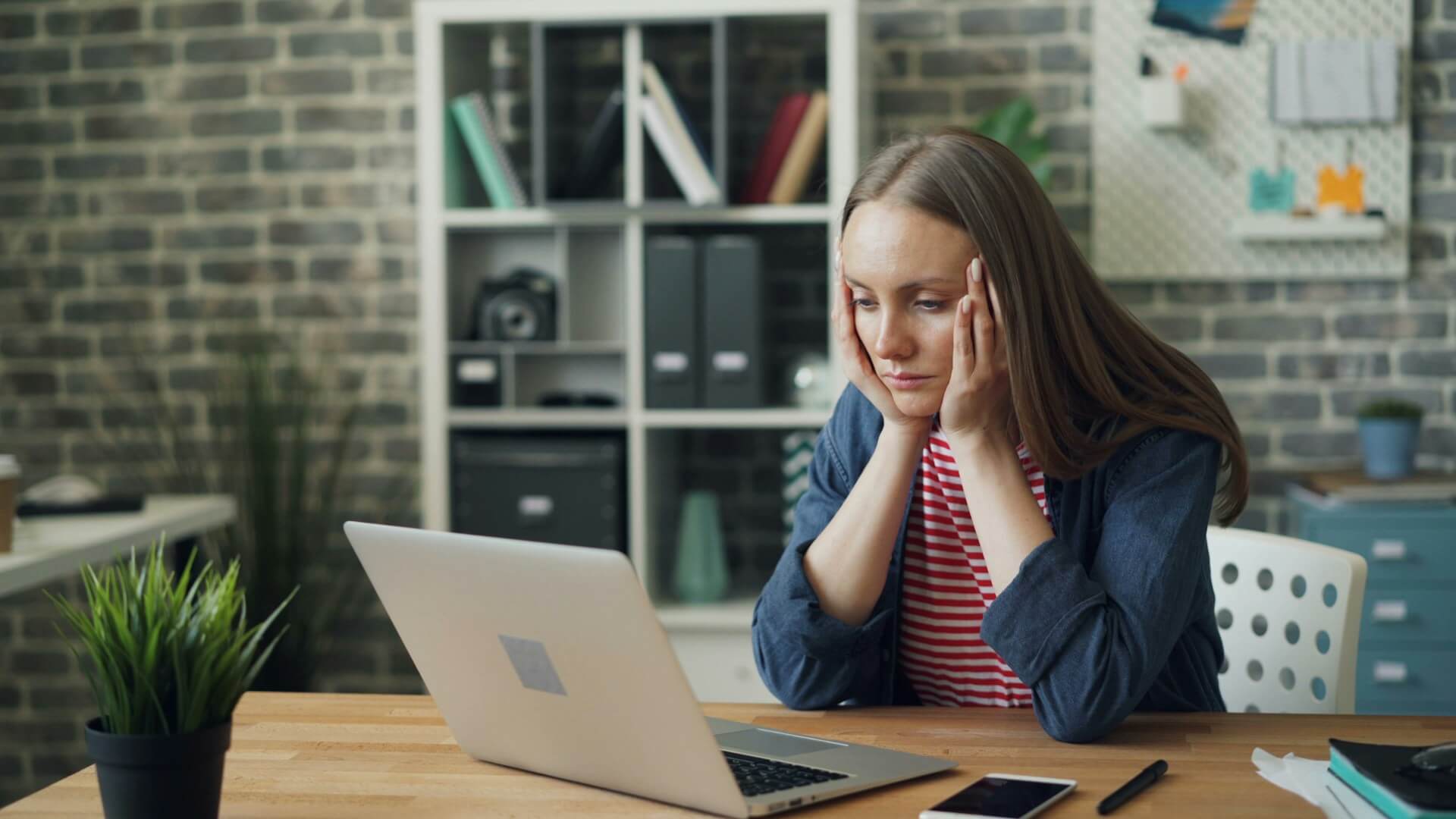 TBC, based on image. For this: Tired young woman sat at a desk looking at her laptop, while holding her head with both hands.